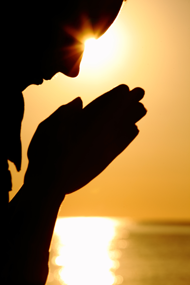 Silhouette of man praying at sunset near ocean