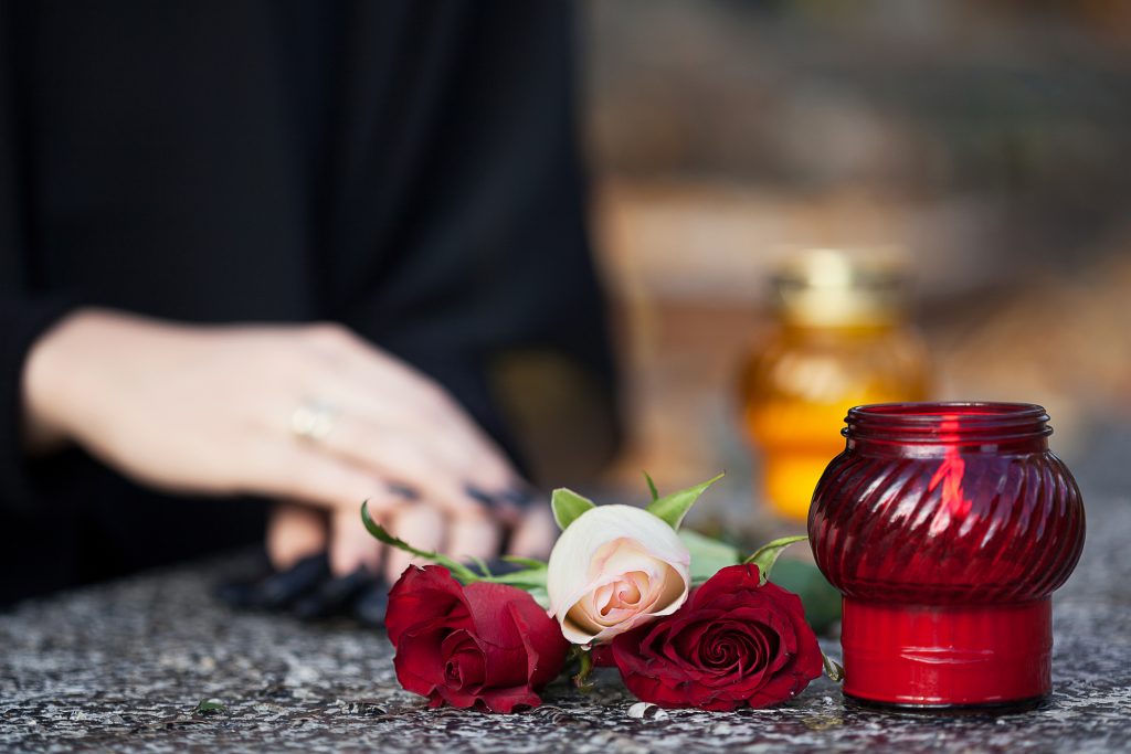 Woman in mourning arranging flowers and candles on the gravestone