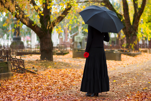 Woman standing in a cemetery holding an umbrella