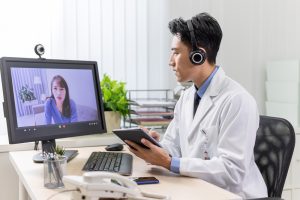 Telemedicine concept - asian male doctor has video call with female patient with depression online by webcam in clinic