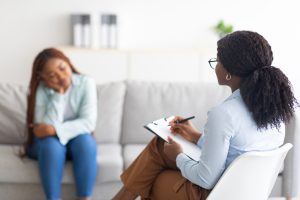 Depressed black lady receiving professional psychological help at mental clinic, selective focus. Female psychotherapist having session with desperate Afro lady with ptsd or emotional trauma