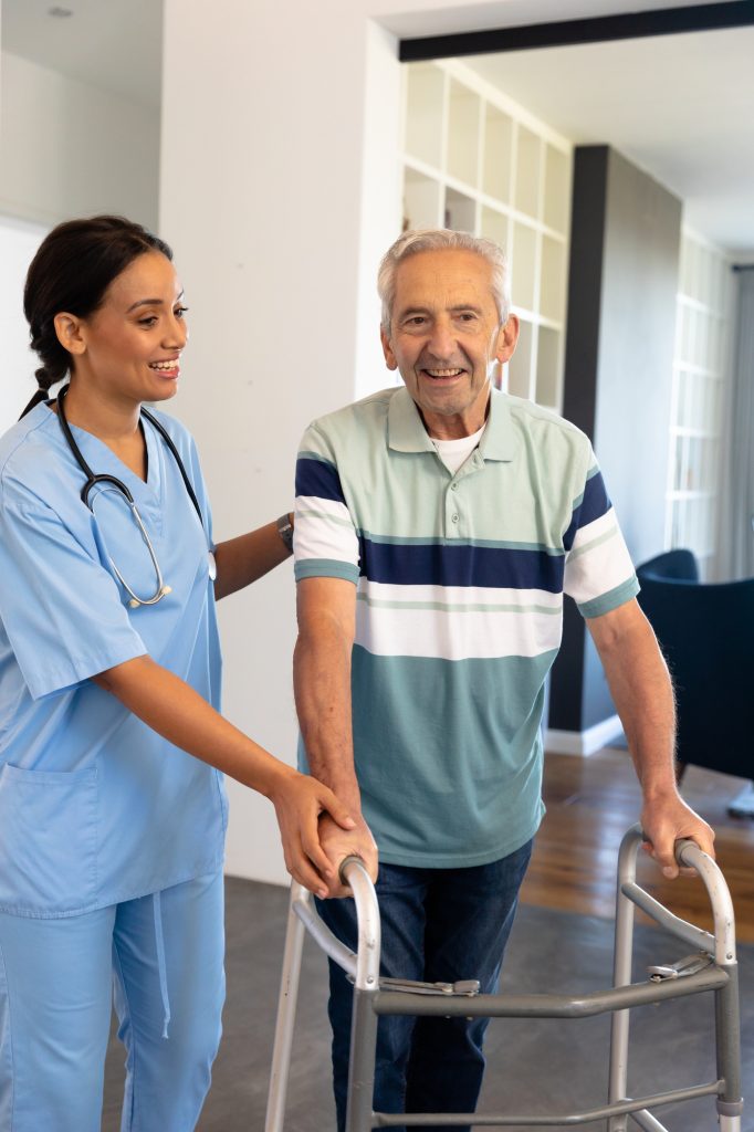 Smiling multiracial female physiotherapist assisting senior man in walking with walker at home. Unaltered, physical therapy, healthcare, patient, retirement, recovery, support, disability concept.