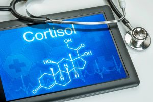 photo of an Apple I PAD and a stethoscope, the Word Cortisol is written on the I PAD with a blue background and the chemical formula for Cortisol is shown