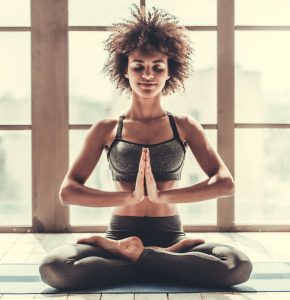 A woman meditating indoors with her legs crossed and hands together. 