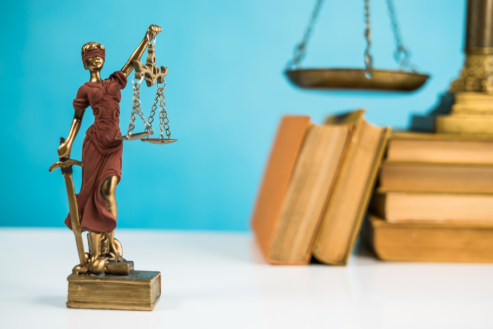 A statue of lady justice hold a scale next to law books