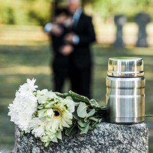 A couple standing behind a grave stone with flowers and an urn on it
