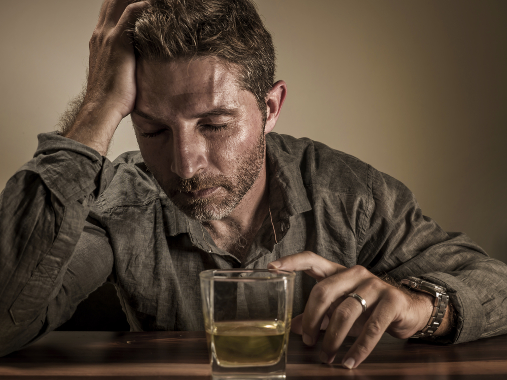 Attractive desperate alcoholic man . depressed addict isolated in front of whiskey glass drunk and wasted in dramatic expression suffering alcoholism and alcohol addiction problem