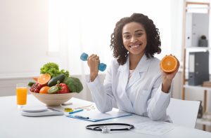 A nurse sitting at a table smiling while holding an orange and reviewing a file.