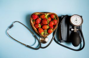 The concept of health. Fresh strawberries with a stethoscope and a pressure measuring device on a blue background, top view