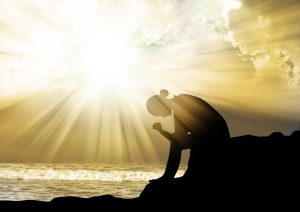 A woman praying at the beach with the sun behind her