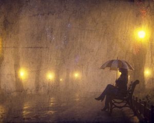A woman alone in the rain sitting on a bench with an umbrella at night