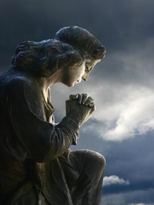 A statue of a person praying on a cloudy day