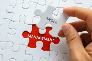 Hand holding piece of blank jigsaw puzzle with word ANGER MANAGEMENT.