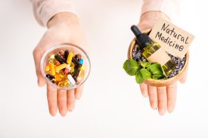 2 hands. One has pills and the other has holistic nursing natural medicine herbs.
