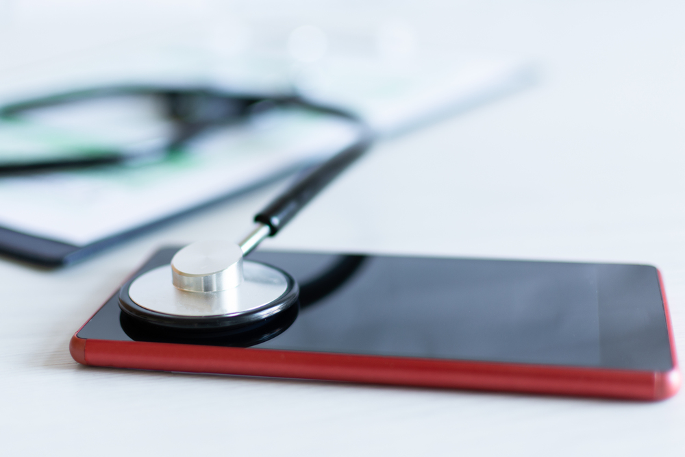 Stethoscope on red smartphone on a grey background. Calling for doctor appointment concept or phone repair service concept.