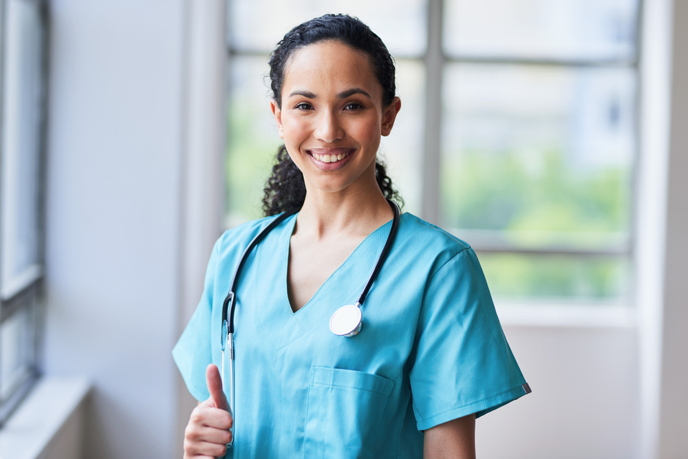 Portrait of a confident female doctor in scrubs, smiling and giving a thumbs up. The image captures the positive, professional healthcare environment in a hospital setting.