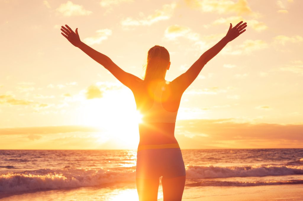 Woman with arms stretched out looking at a sunset on a beach