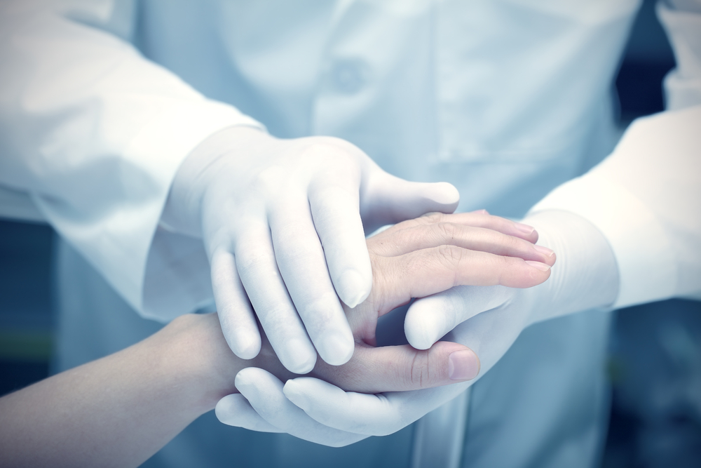 Doctor holding hands with a patient while wearing gloves. 
