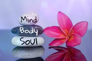 A pretty flower next to stones that have Mind, Body, Soul painted on them. 