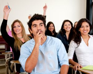 A classroom full of young nursing students with their hands raised. 
