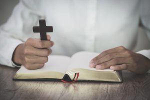 A person reading the bible while holding a cross