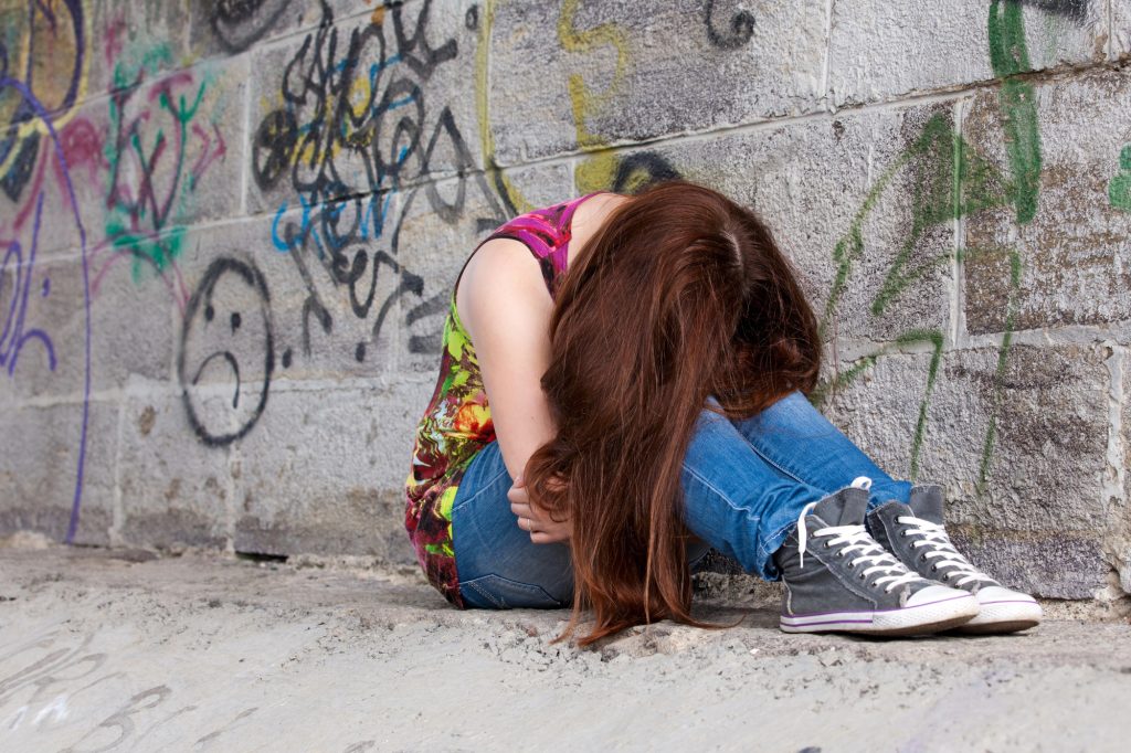 Teenage girl sitting on the ground next to a brick wall. 