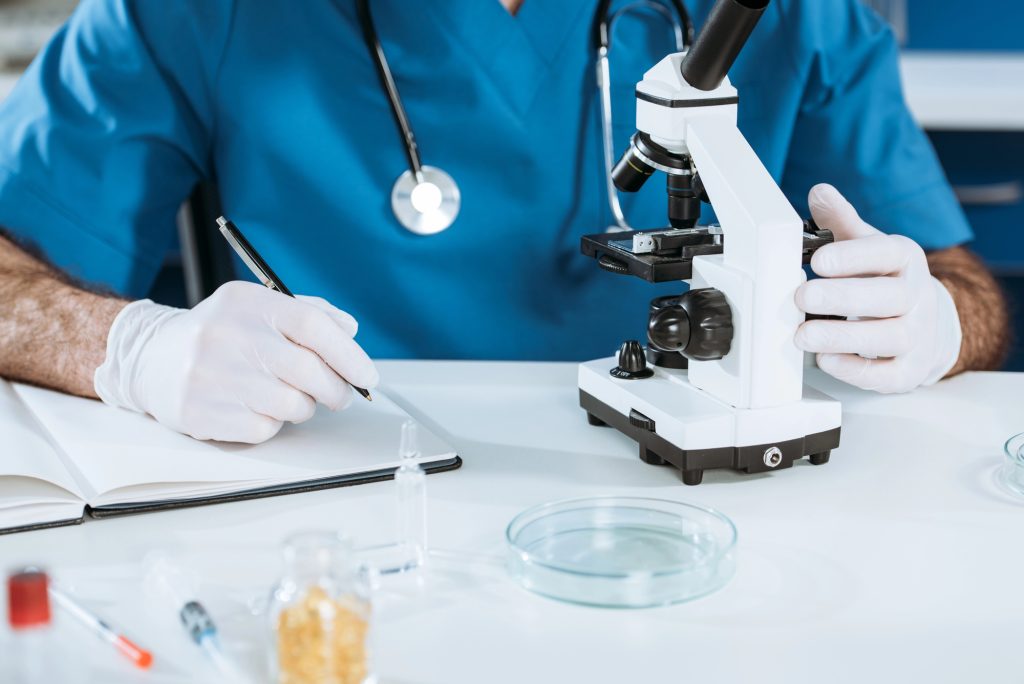 Cropped view of biologist in latex gloves holding glass container with vaccine near test tubes