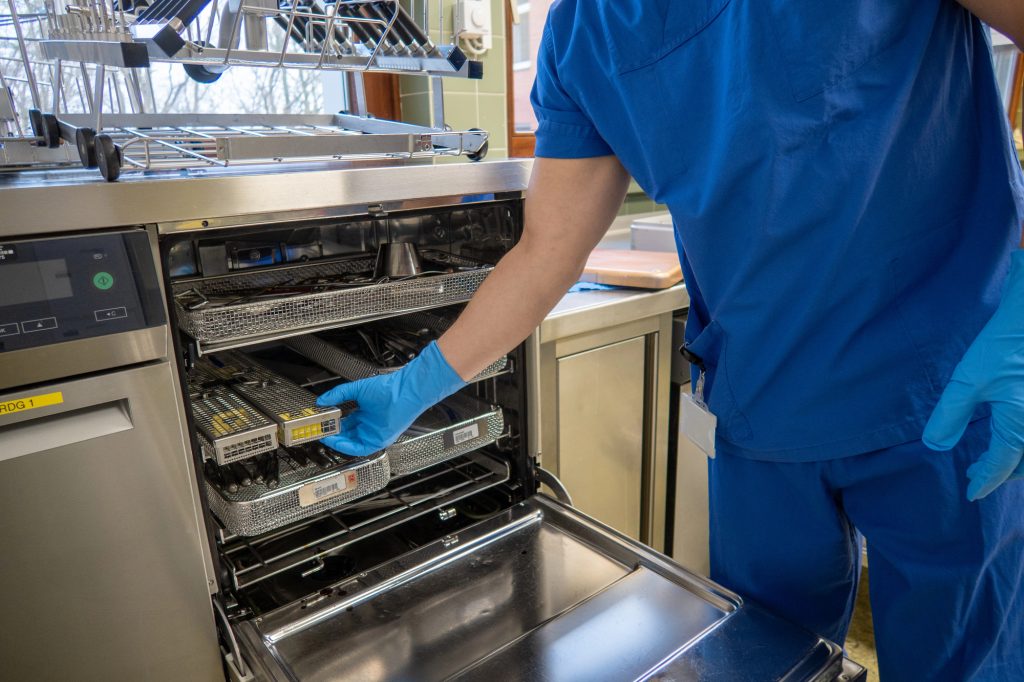 An employee of a surgical department loads a washing machine with used surgical instruments