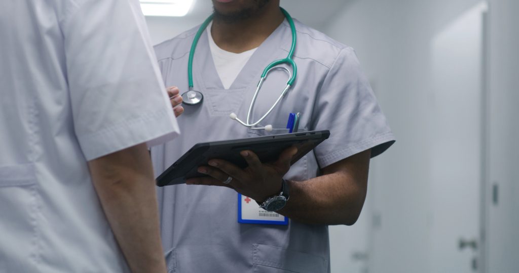 African American medic shows medical test results on digital tablet computer to another doctor. Multicultural doctors discuss ways of treatment in middle of hospital corridor. Medical staff at work.