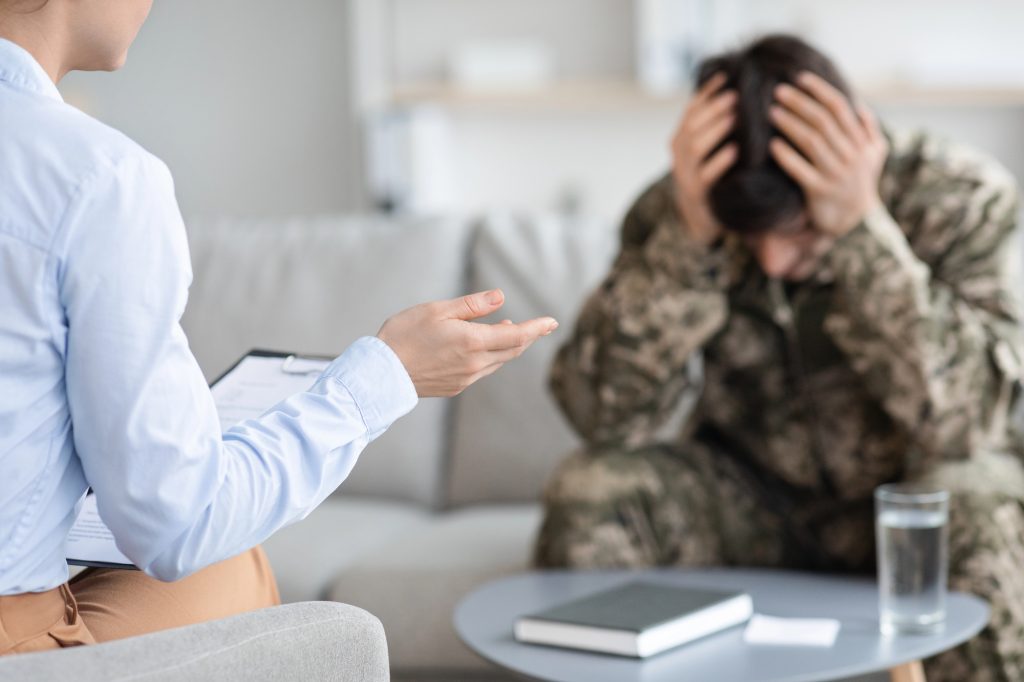 Unrecognizable lady psychologist having conversation with soldier who is unhappy about his sessions not being covered by insurance due to lapse authorization. 
