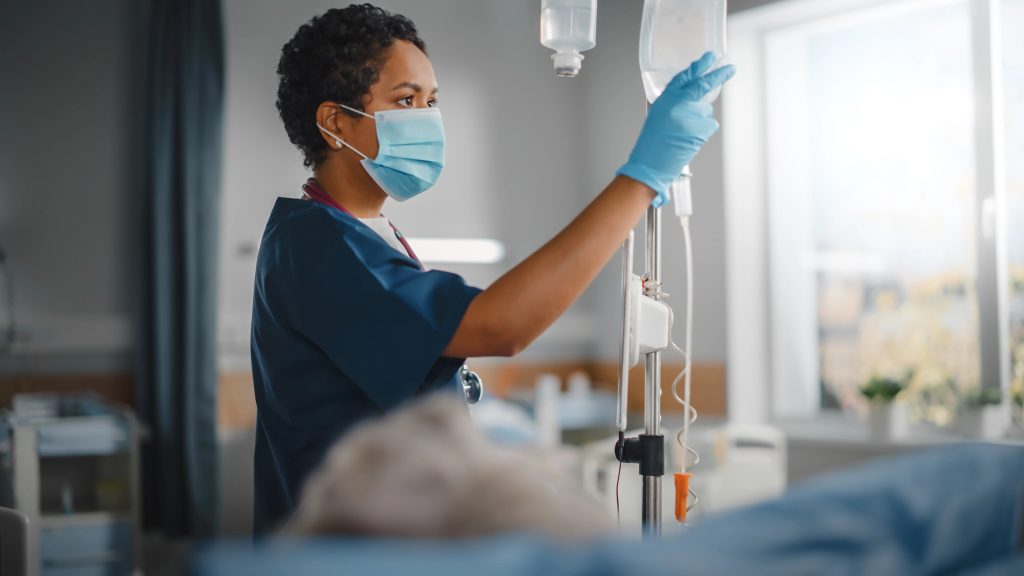 Hospital Ward: Professional Black Head Nurse Wearing Face Mask Does Checkup of Patients Vitals, Checking Heart Rate Computer, Intravenous or Iv Fluids Drip Bag.
